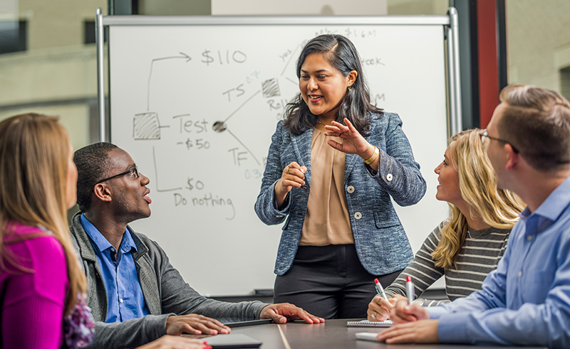 A female WSB professor talking with a group of students in front of a whiteboard