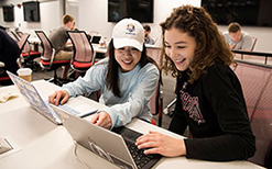 Two female students work on their laptops in the WSB Learning Commons