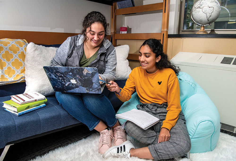 Roommates Jaqueline Sanchez and Hannah Brennan look at a laptop in their dorm room